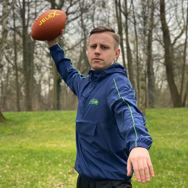 Mann in blauer Jacke hält JELEX American Football hoch im Wald