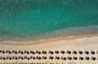 Luftaufnahme eines Strandes mit türkisfarbenem Wasser und Reihen von Sonnenschirmen