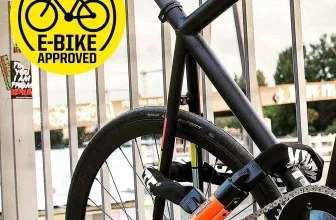 Schwarzes E-Bike mit orangefarbenem Kryptonite Kabelschloss, das um Rahmen und Rad gesichert ist.