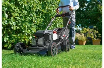 Person schiebt schwarzen Parkside Benzin-Rasenmäher auf grünem Rasen