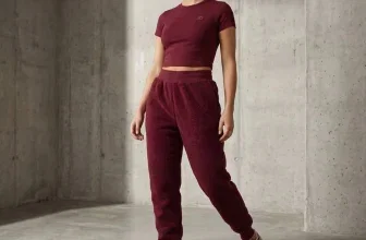 Model in burgunderfarbener PUMA Studio Sherpa Fit Hose und Crop-Top vor Betonwand