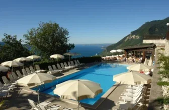 Poolanlage mit Liegestühlen und Sonnenschirmen mit Blick auf den Gardasee und Berge