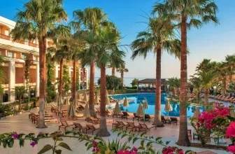Hotelanlage mit Palmen, Swimmingpool und Liegestühlen unter blauem Himmel
