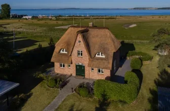 Luftaufnahme eines Ziegelhauses mit Strohdach und Grünfläche am Meer
