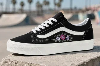Schwarzer Vans Old Skool Sneaker mit Blumenstickerei auf Betonkante vor Skatepark