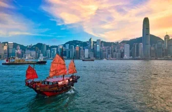 Traditionelles Segelboot mit roten Segeln vor der Skyline von Hongkong bei Sonnenuntergang