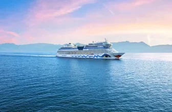 AIDA-Kreuzfahrtschiff auf offener See bei Sonnenuntergang mit Bergkulisse im Hintergrund