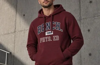 Mann in bordeauxrotem Hoodie mit Bench-Logo vor Betonwand