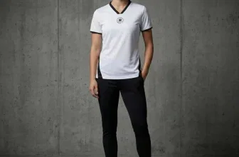 Model in weißem DFB-Trikot mit schwarzem Kragen und schwarzen Leggings vor grauer Wand
