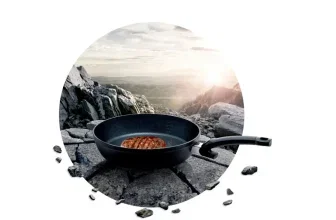 Schwarze Pfanne mit Steak auf Felsbrocken in Berglandschaft bei Sonnenuntergang