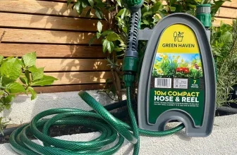 Grüne Gartenschlauchtrommel von Green Haven mit Sprühkopf und aufgewickeltem Schlauch vor einer Holzwand.