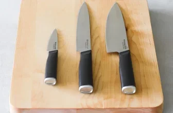 Drei KitchenAid Küchenmesser mit schwarzen Griffen auf einer hellen Holzschneideplatte
