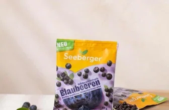 Seeberger-Beutel mit gefriergetrockneten Blaubeeren auf Holz, daneben frische Beeren in einer Schale