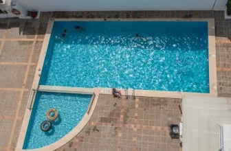 Luftaufnahme des Hotel-Pools mit blauem Wasser, zwei Schwimmringen und Personen am Beckenrand