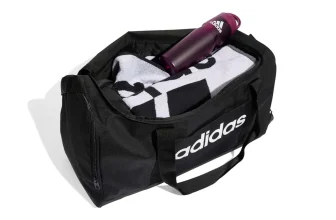 Schwarze adidas Sporttasche mit geöffnetem Deckel, darin liegen ein weißes Handtuch und eine lila Flasche.