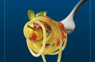 Gabel mit Spaghetti, Tomatenstücken und Basilikum vor blauem Hintergrund mit Text Immer Al Dente