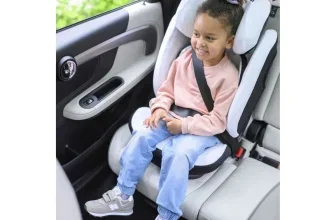 Kind mit rosa Oberteil und Jeans sitzt in einem weißen Maxi-Cosi Kindersitz im Auto.